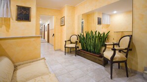 Un hall d’hôtel avec un comptoir d’accueil, deux fauteuils, un grand miroir et une plante en pot.