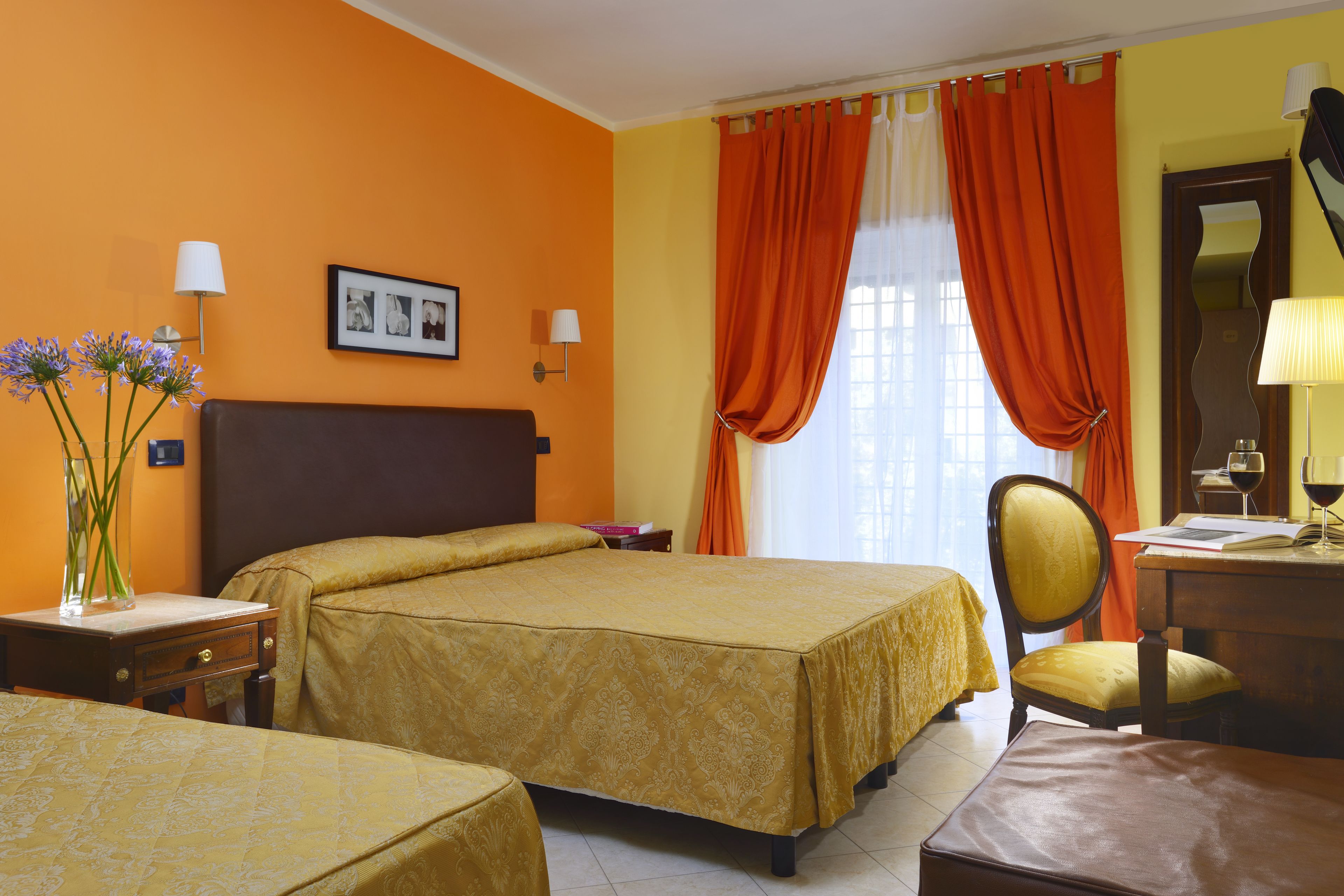 A hotel room with two beds, a desk, a chair, and a mirror.