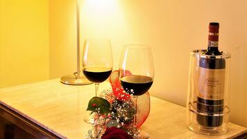 Una mesa con dos copas de vino, una botella, una lámpara y un arreglo floral decorativo.