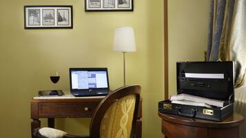 A room with a desk, laptop, open briefcase, chair, lamp, and framed pictures on the wall.