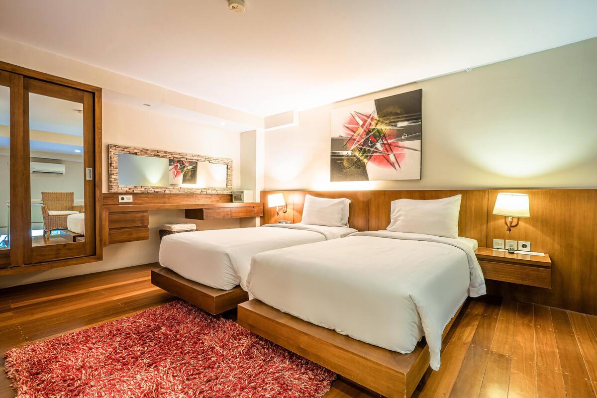A hotel room with two beds, a large mirror, a wooden headboard, and a red rug.