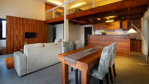 A modern living room with a wooden dining table, patterned chairs, a sofa, and a kitchen area with a tiled backsplash. - Pandawa All Suite Hotel (Kerobokan)