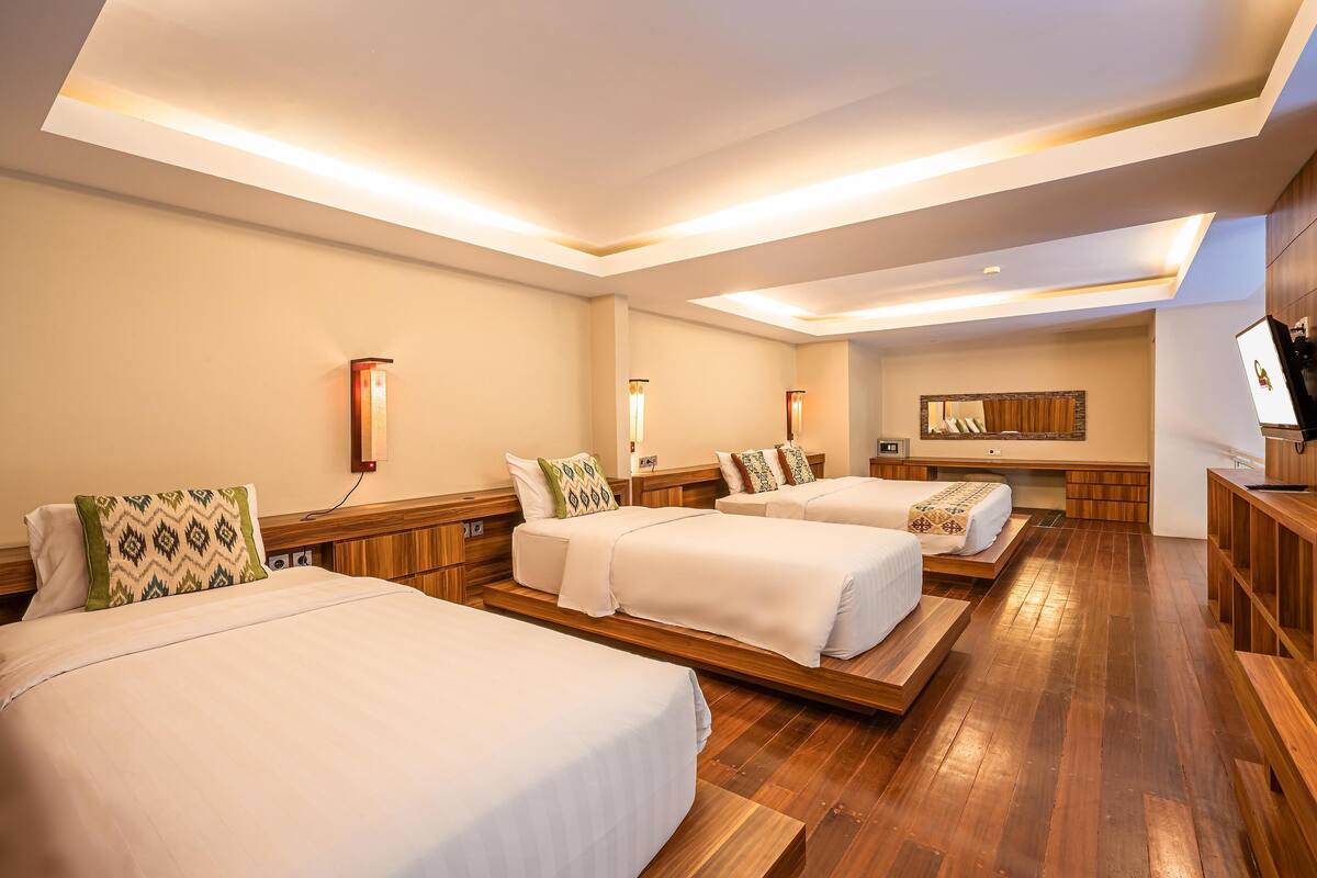 A hotel room with three beds, wooden flooring, and built-in shelves.
