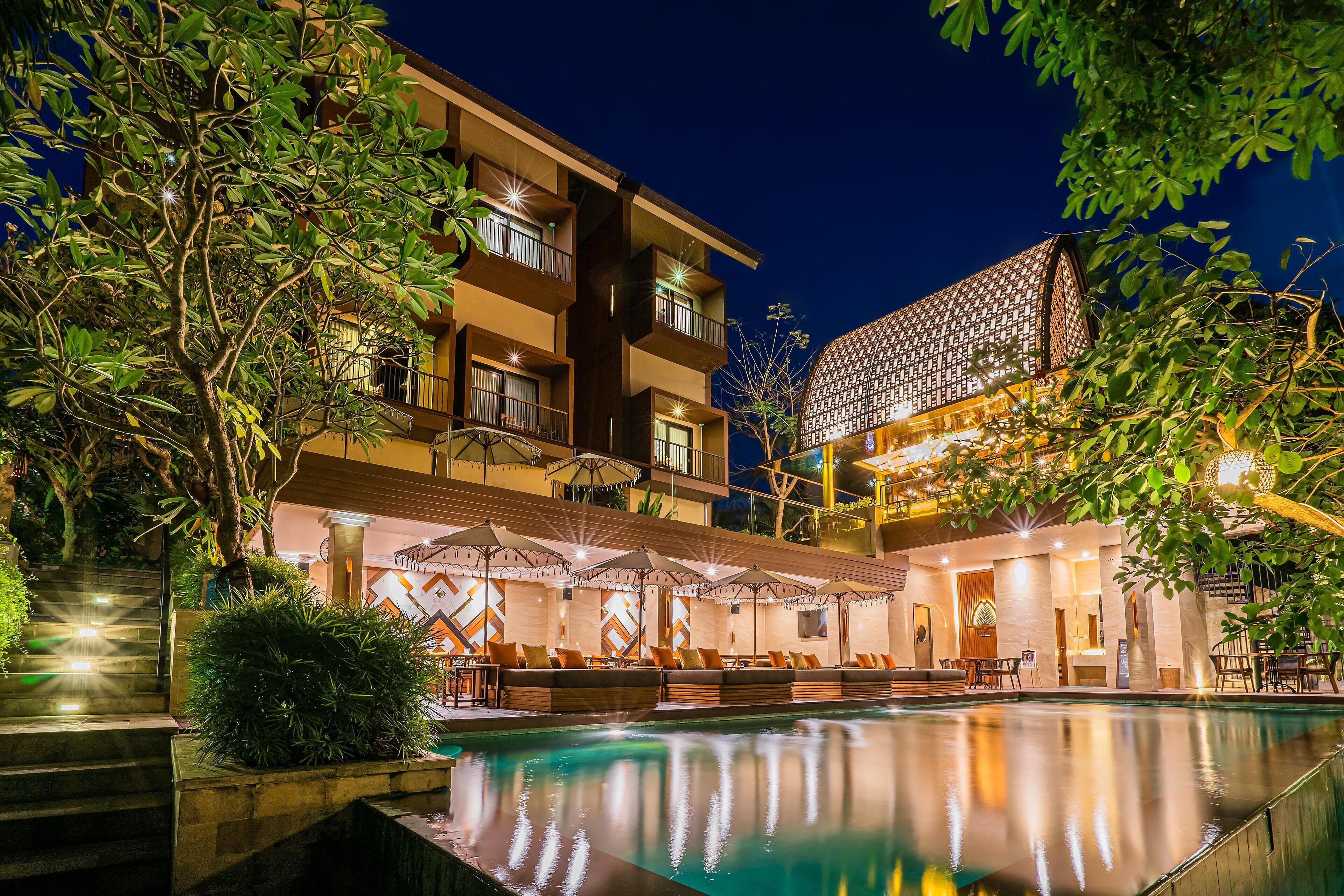 A hotel with a swimming pool, outdoor seating, and a well-lit facade.