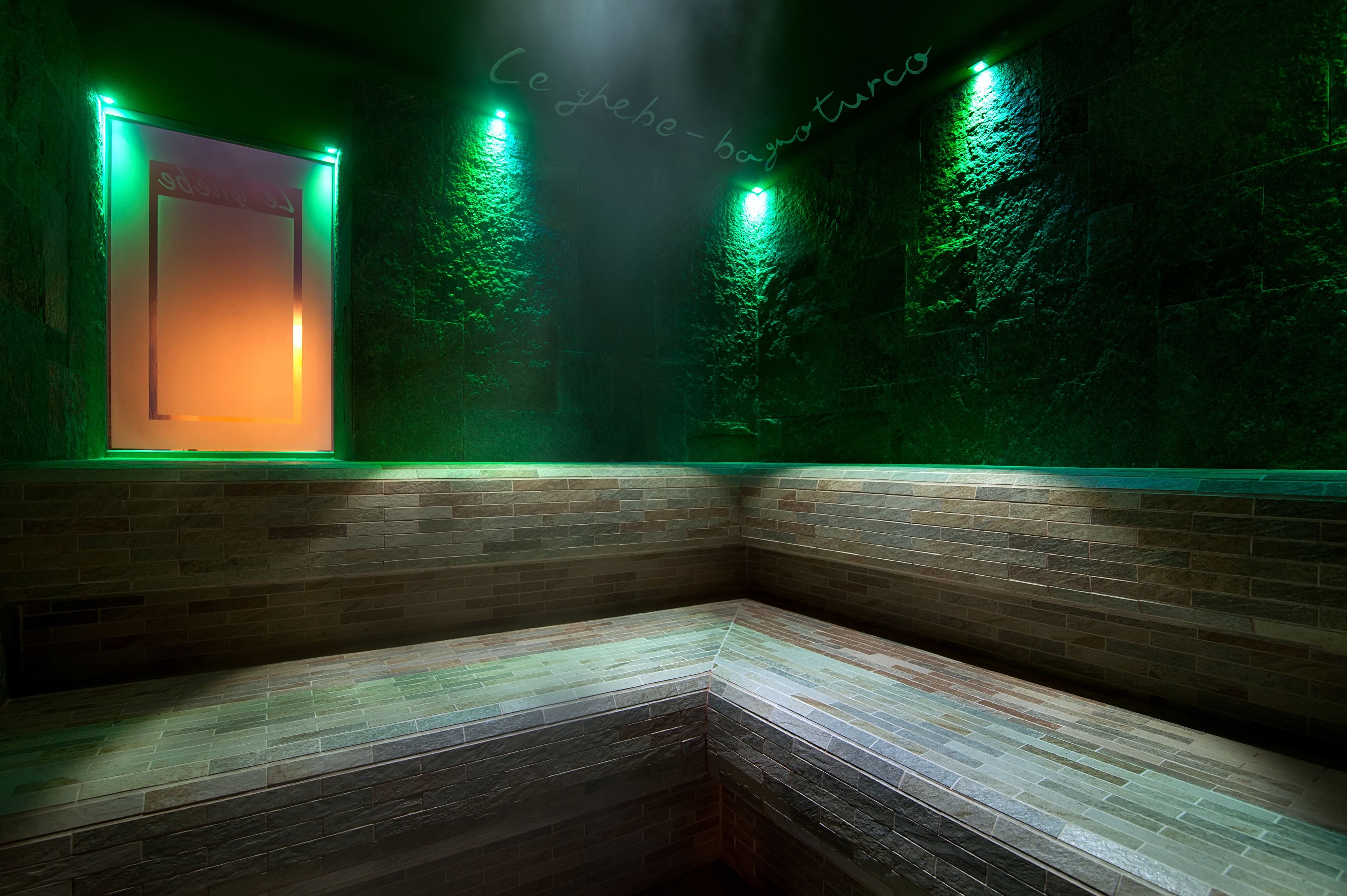 Une pièce faiblement éclairée, avec un mur illuminé de lumière verte et un espace avec des bancs.