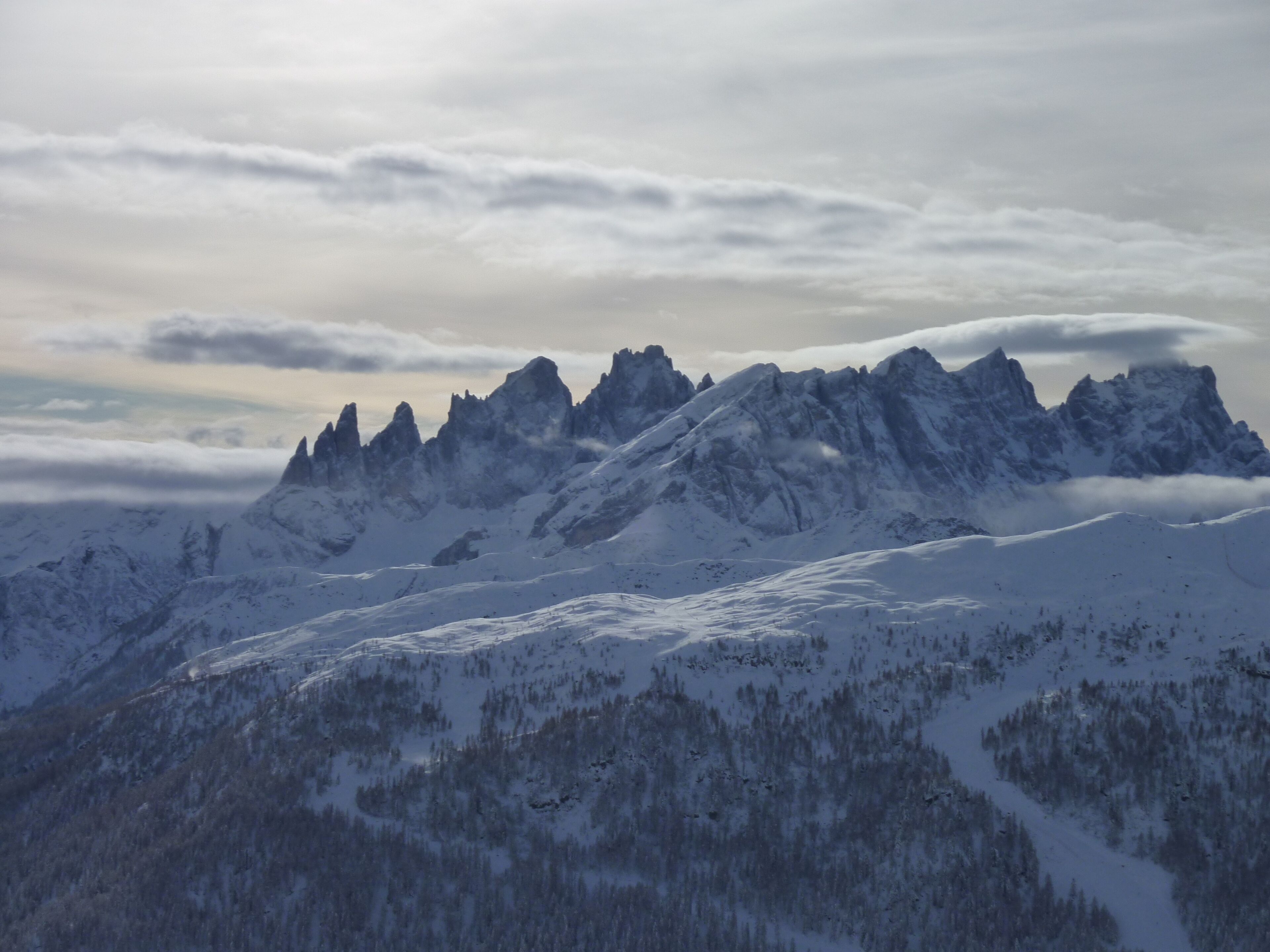 Ein verschneites Gebirge mit schroffen Gipfeln und einem bewaldeten Tal.