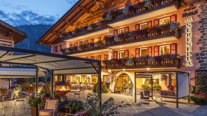 Un hotel de varios pisos con balcones decorados con flores, mobiliario exterior y fachada de piedra.