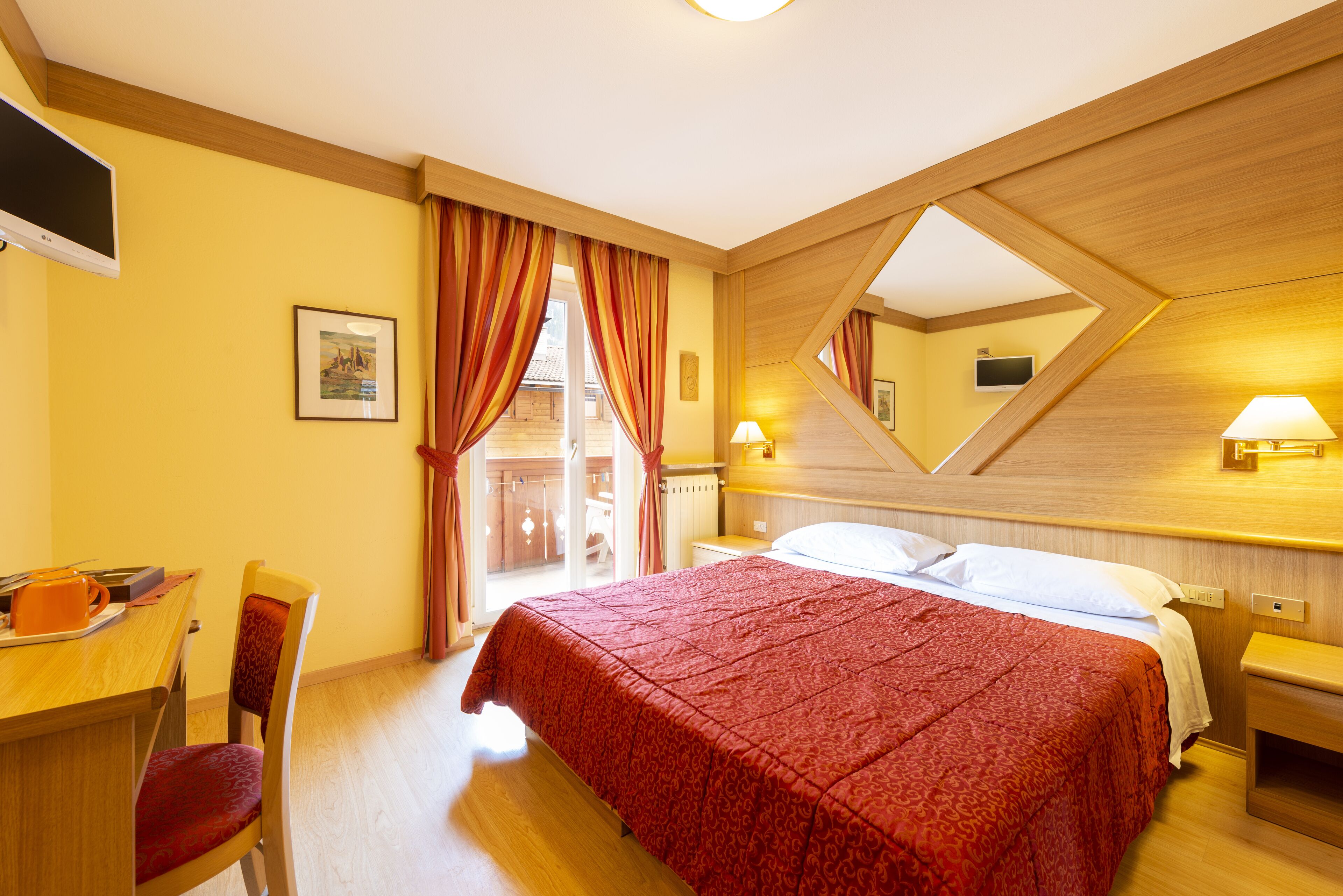 A hotel room with a bed, a desk, a chair, a TV, and a window with curtains.