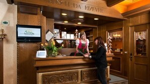 Un mostrador de recepción con detalles de madera, una pantalla digital que muestra información del hotel y una planta decorativa.