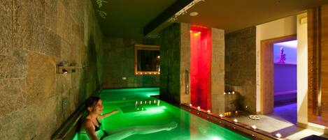 A spa area with a large soaking tub, stone walls, and a red-lit wall.