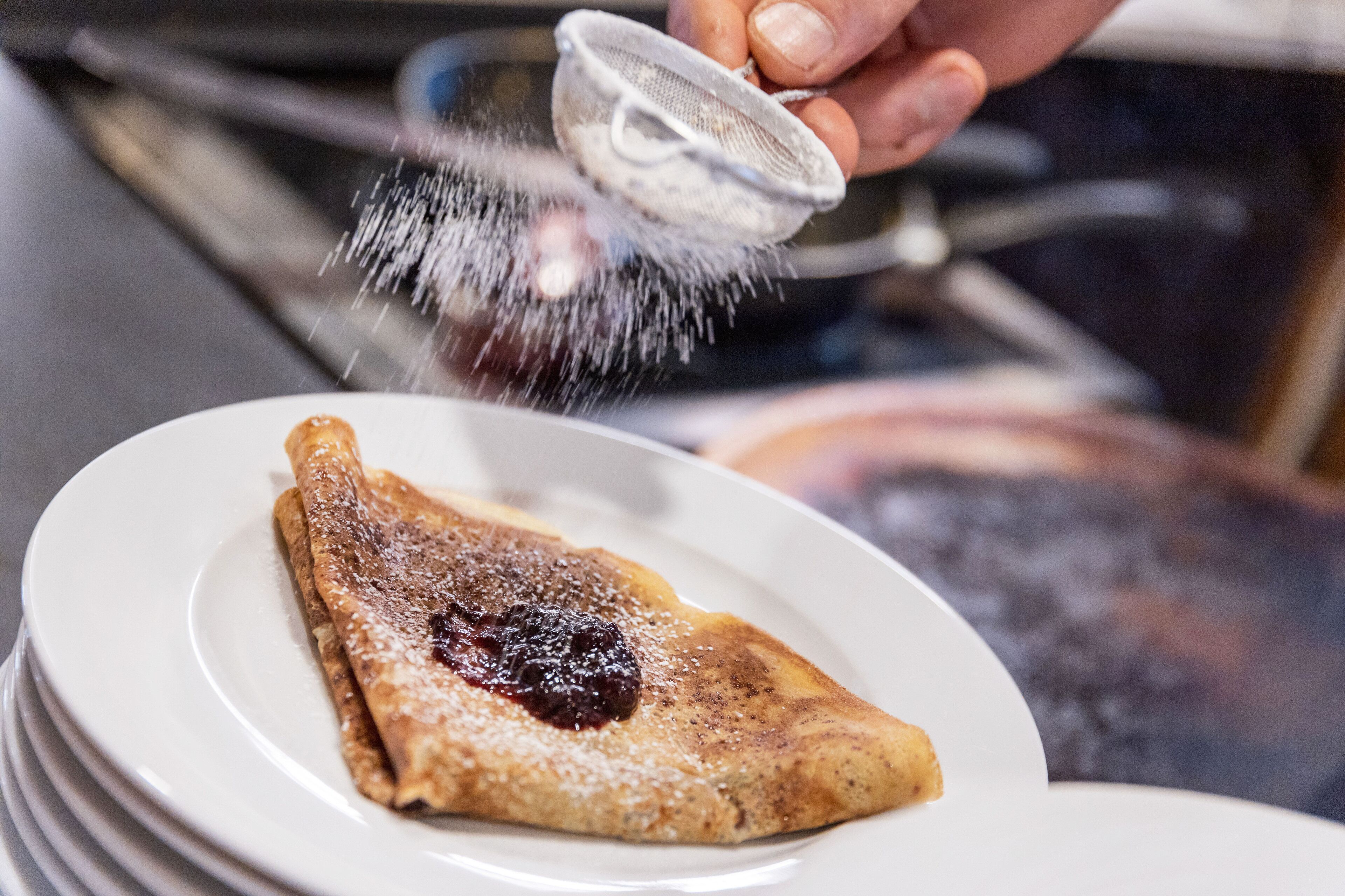 A stack of white plates with a crepe topped with powdered sugar and a red sauce.