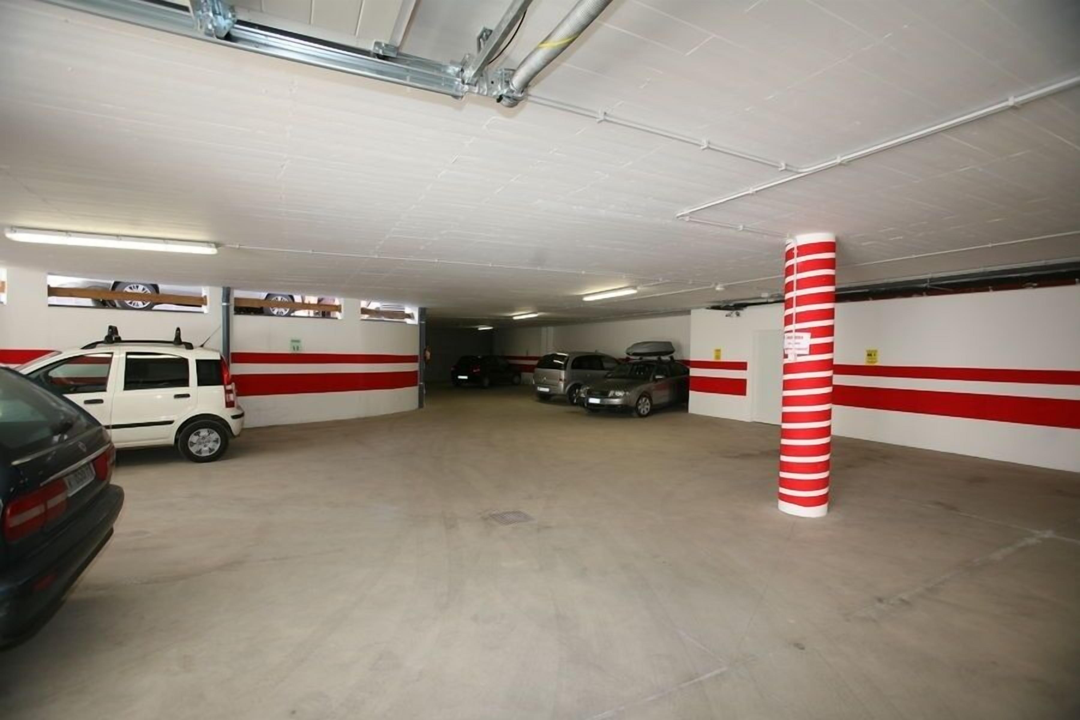 Eine Parkgarage mit weißen und roten Wänden, Betonboden und mehreren stehenden Autos.