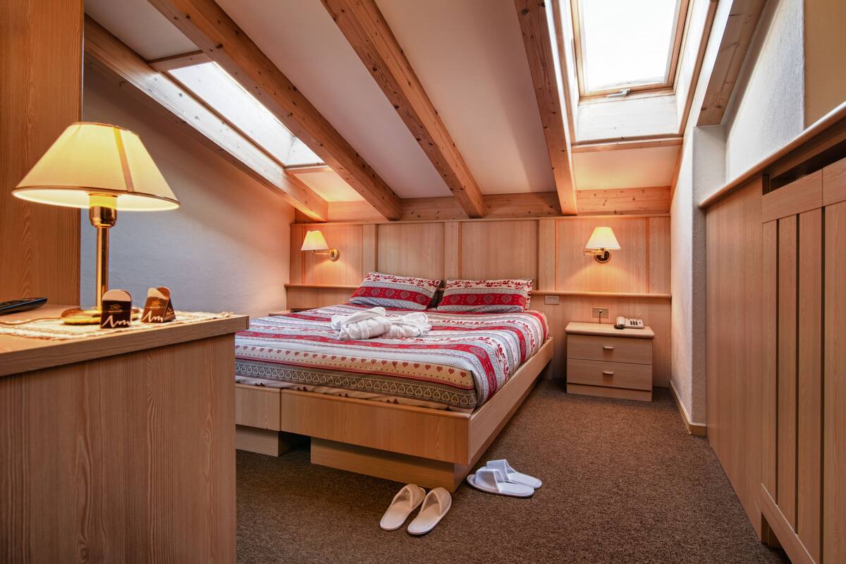 A cozy bedroom with a wooden bed, bedside lamps, and a skylight.