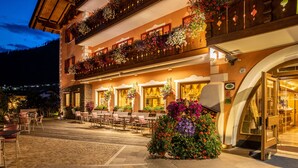 Un hotel con asientos exteriores, un balcón lleno de flores y vistas a las montañas.