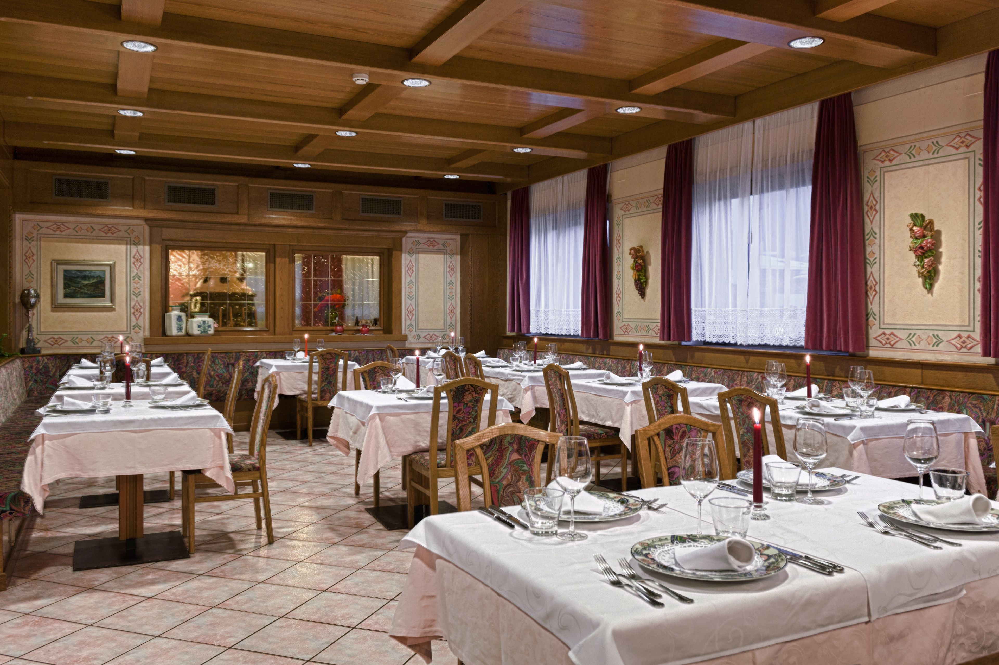 A dining area with multiple tables set for service, wooden ceiling beams, and patterned wall decorations.