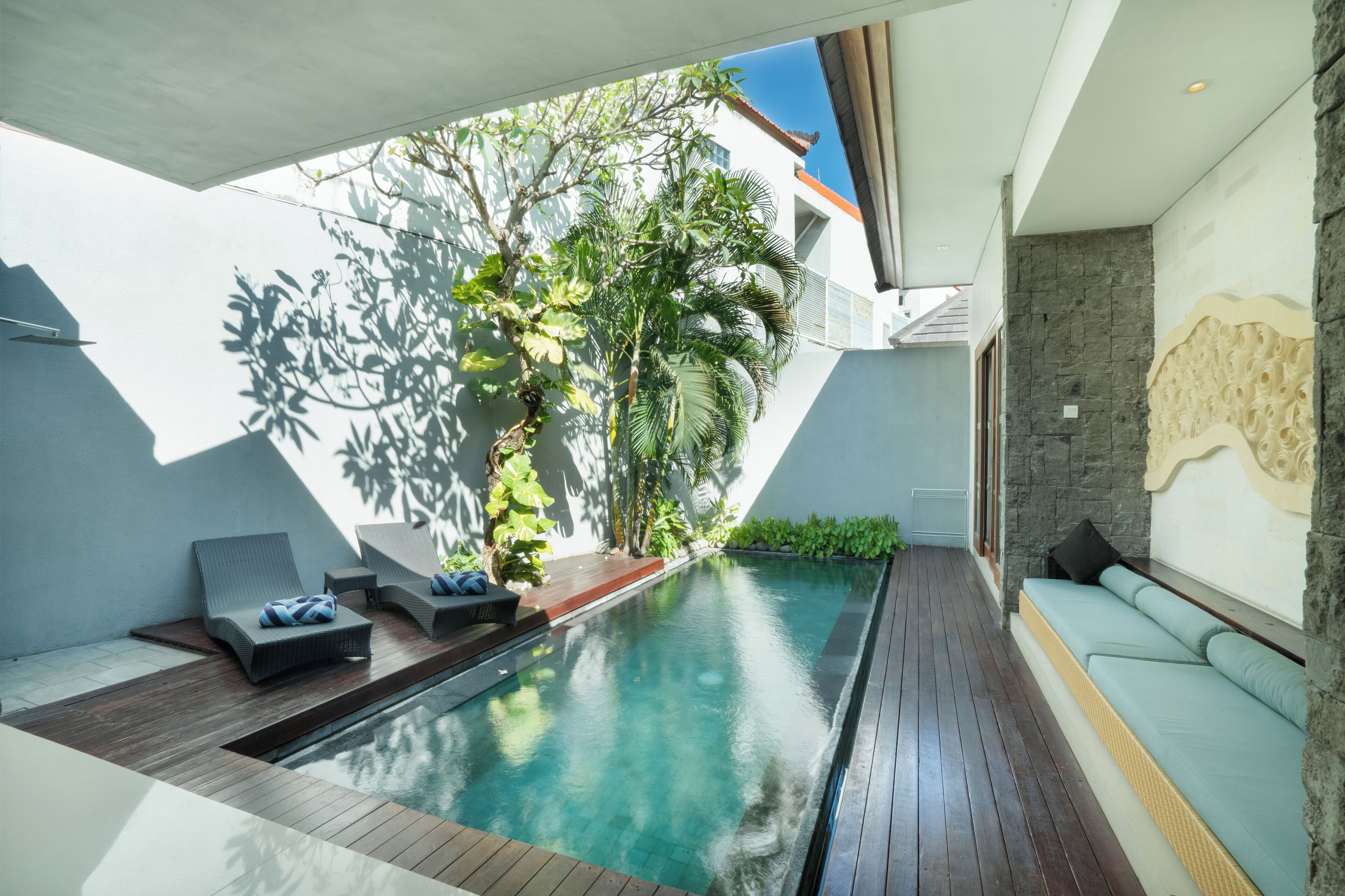 A modern indoor pool area with wooden flooring, lounge chairs, and a stone wall.