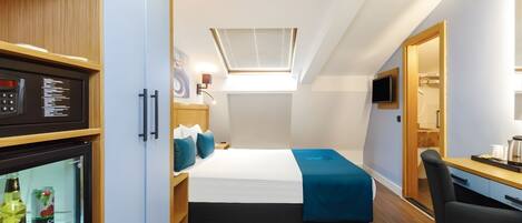 A compact hotel room with a bed, a desk, a chair, a mini-fridge, and a TV.