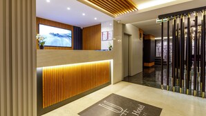 A modern hotel reception area with a wooden reception desk, a digital screen, and a marble floor with a hotel logo.