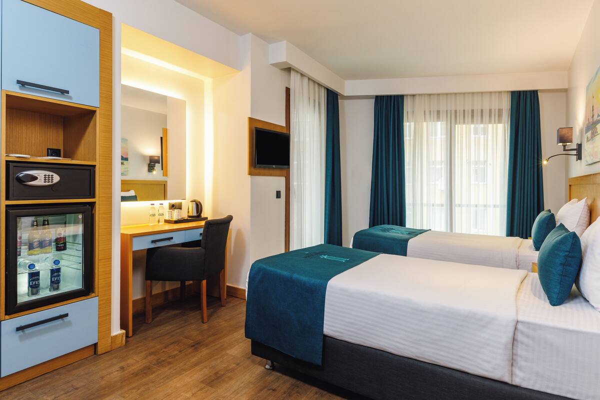 A hotel room with a desk, two beds, a minibar, and a television.