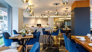 A modern dining area with blue upholstered chairs, wooden tables, and pendant lighting. - Urban Hotel Bomonti (Istanbul)
