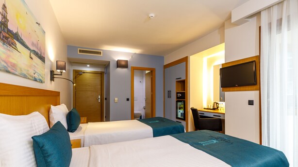 A hotel room with two beds, a desk, a TV, and a painting on the wall. - Urban Hotel Bomonti (Istanbul)