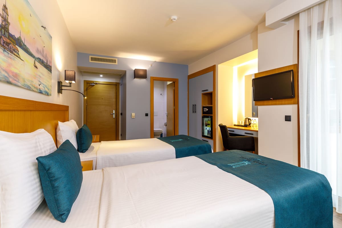 A hotel room with two beds, a desk, a TV, and a painting on the wall.