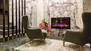 A modern lobby with marble walls, a fireplace, and two grey armchairs.