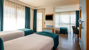 A hotel room with two beds, a TV, a desk, and a view of the city.