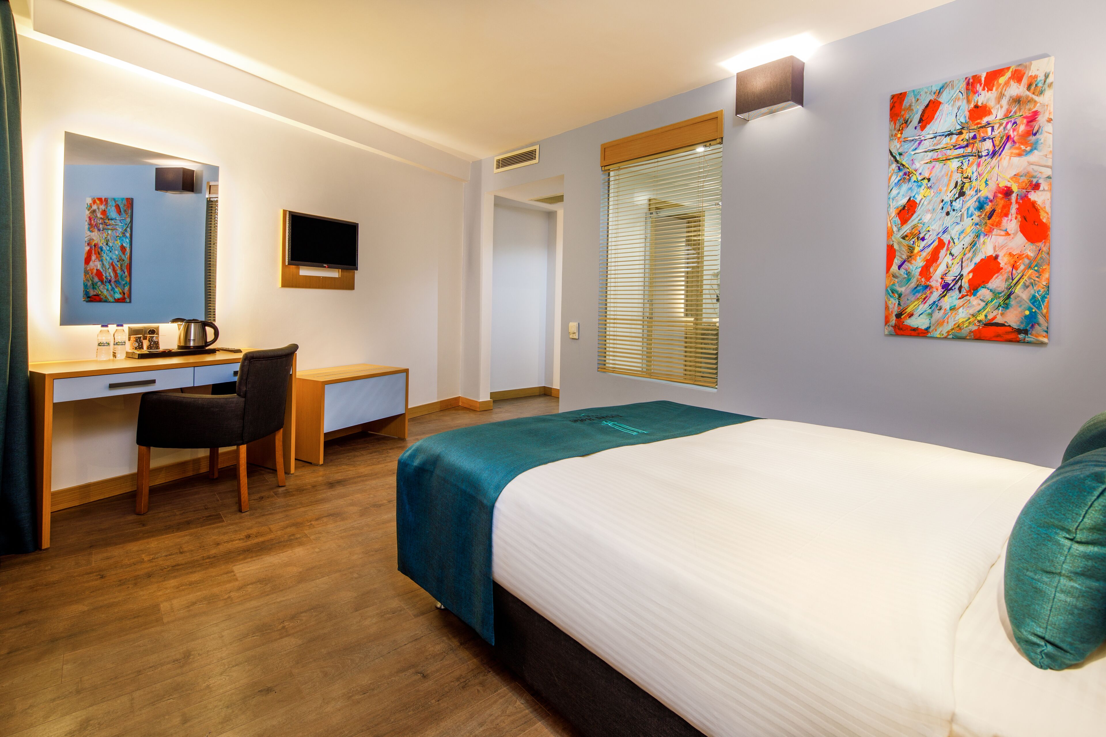 Una habitación de hotel con cama, escritorio, silla, televisor y obras de arte en las paredes.