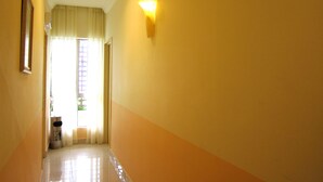 A hallway with a trash bin, a door leading to a room, and a wall-mounted light fixture.