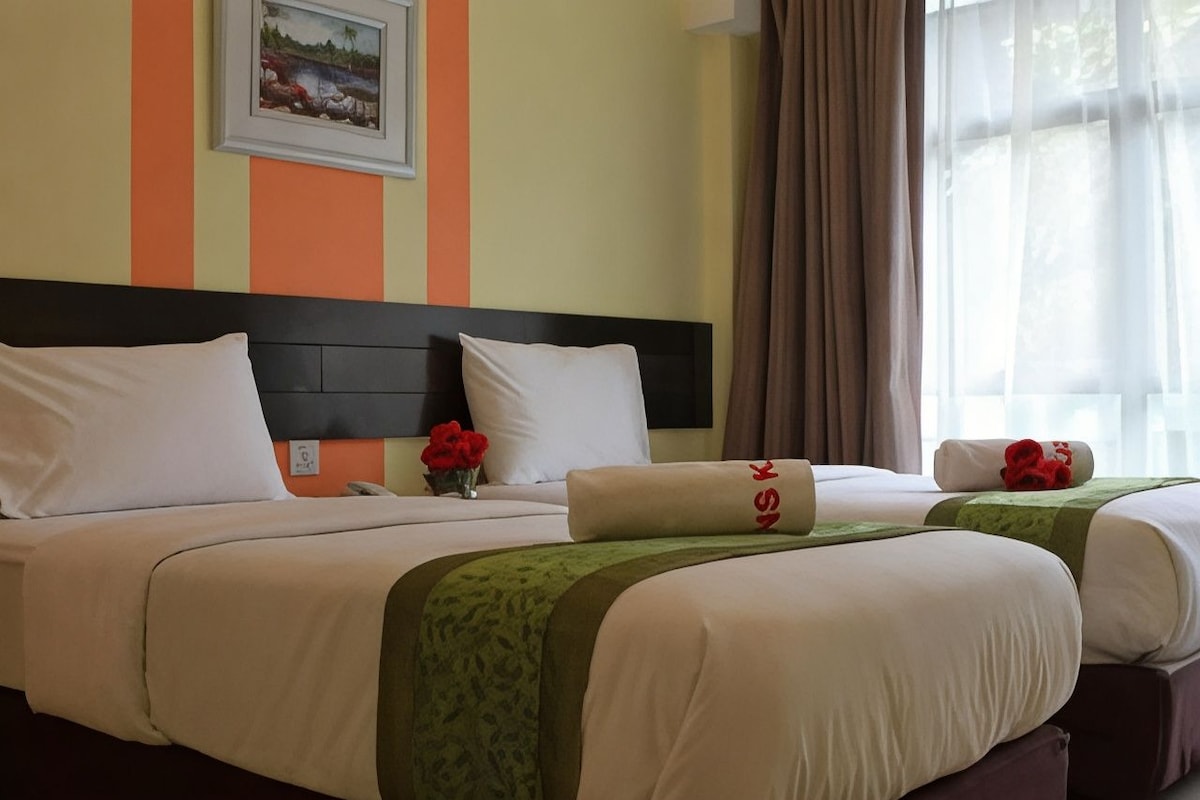 Een hotelkamer met twee bedden, een hoofdeinde, een schilderij aan de muur en een raam met gordijnen.