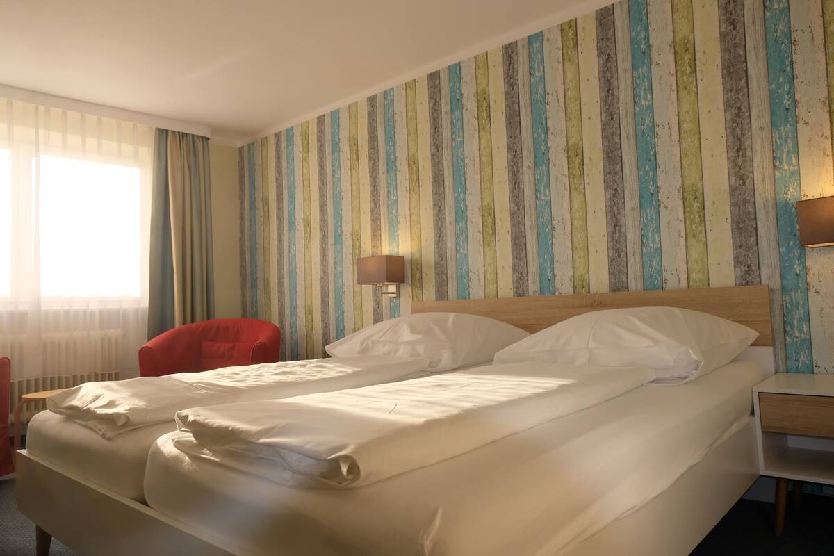 Ein Hotelzimmer mit einem Bett, einem roten Sessel, einem Nachttisch und einer Wand mit Streifenmuster.
