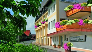 Een hotel met balkonnes versierd met bloemen, een bordje dat aangeeft dat het een restaurant is, en een heldere lucht.