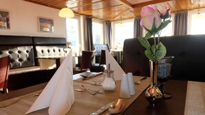 Een eettafel gedekt met een witte servet, bestek, zout- en peperstel, een glazen vaas met een roze roos en een kandelaar.