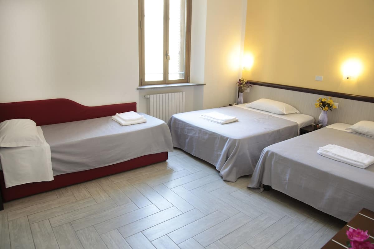 A hotel room with two single beds, a red sofa, a radiator, and a window with natural light.