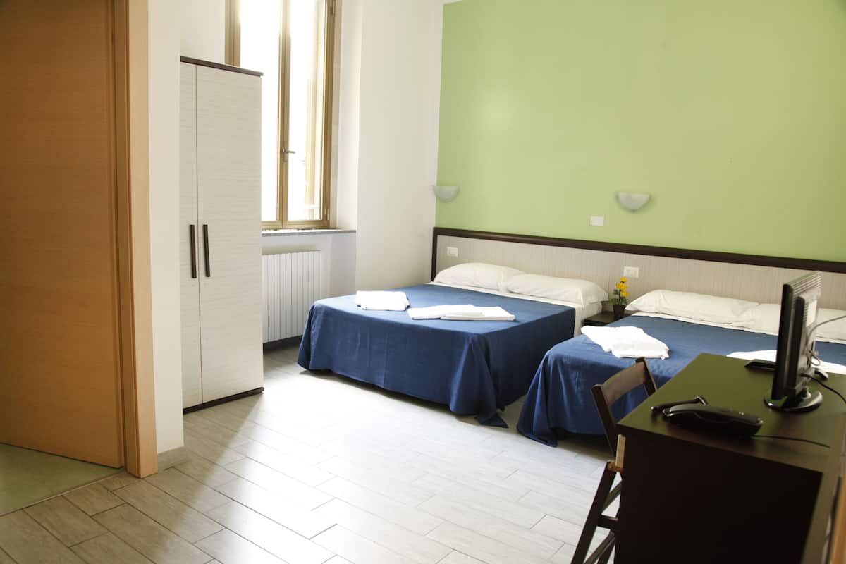 A hotel room with two beds, a desk, a chair, a computer, and a window.