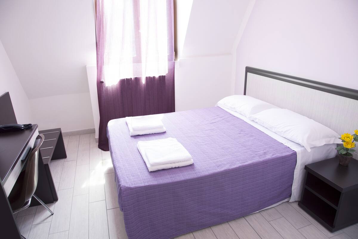 A neatly arranged bedroom with a bed, a desk, and a nightstand.