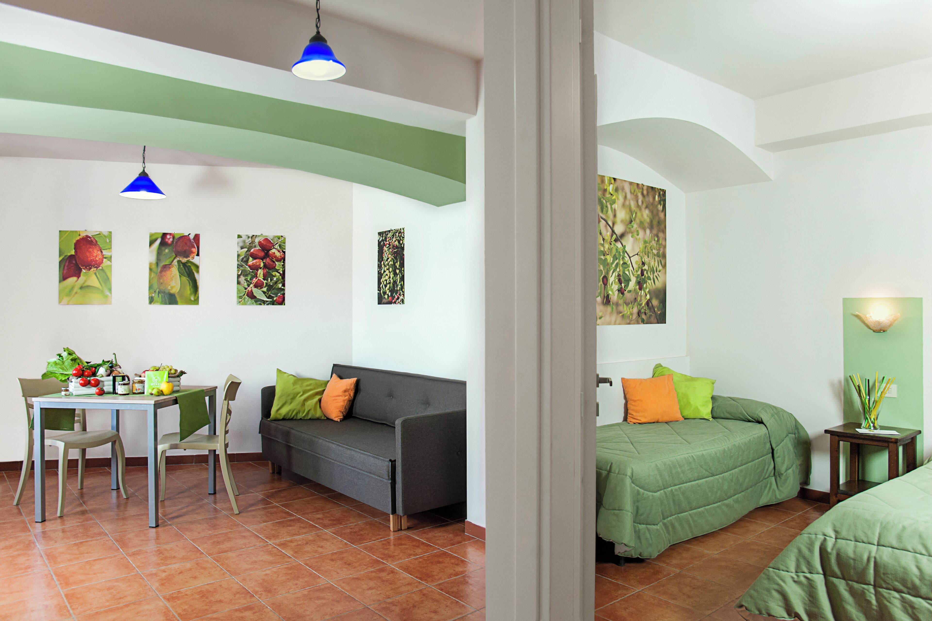 Una habitación con una mesa de comedor, dos sillas, un sofá, una cama con ropa de cama verde y una pequeña mesa con una planta.