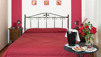 Un letto con una coperta rossa, un comodino con una bottiglia, un vaso con fiori e un piatto con cibo.