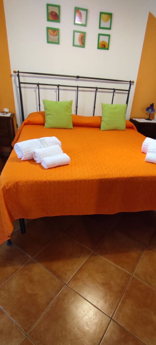 Un letto con copripiumino arancione, cuscini verdi e asciugamani bianchi piegati.