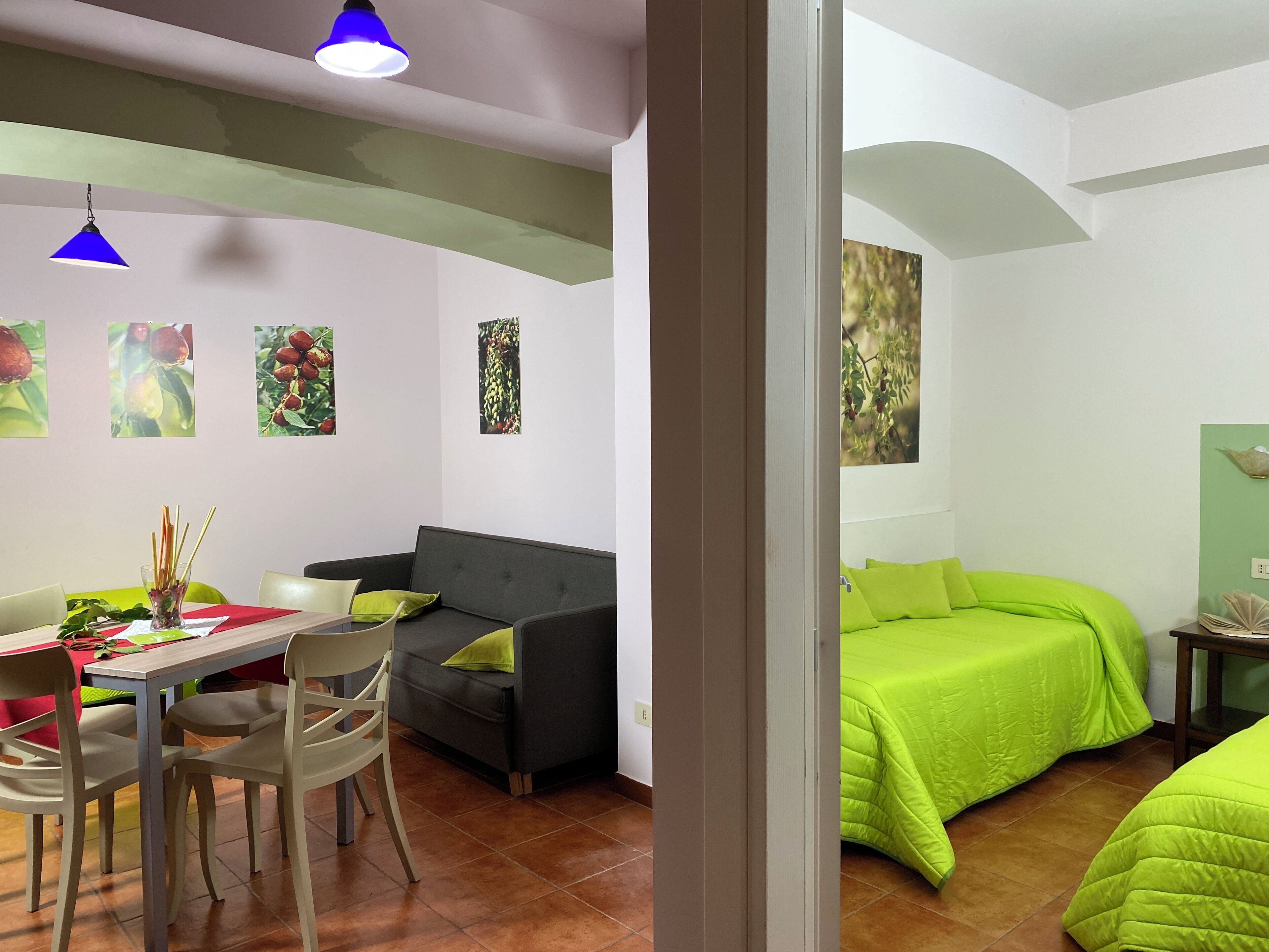 A room with a dining area, a sofa, a bed with green bedding, and wall art.
