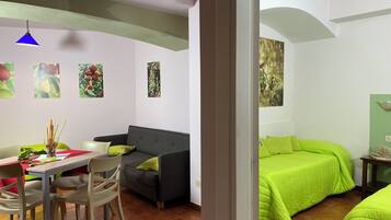 A room with a dining area, a sofa, a bed with green bedding, and wall art.