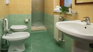 A bathroom with a toilet, bidet, sink, and a glass shower enclosure.