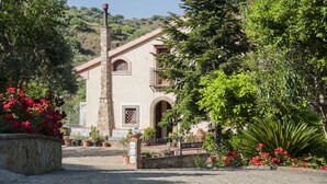 A building with a stone facade, arched windows, and a chimney. There are potted plants and flowers in front of the building. - Agriturismo Bergi (Castelbuono)