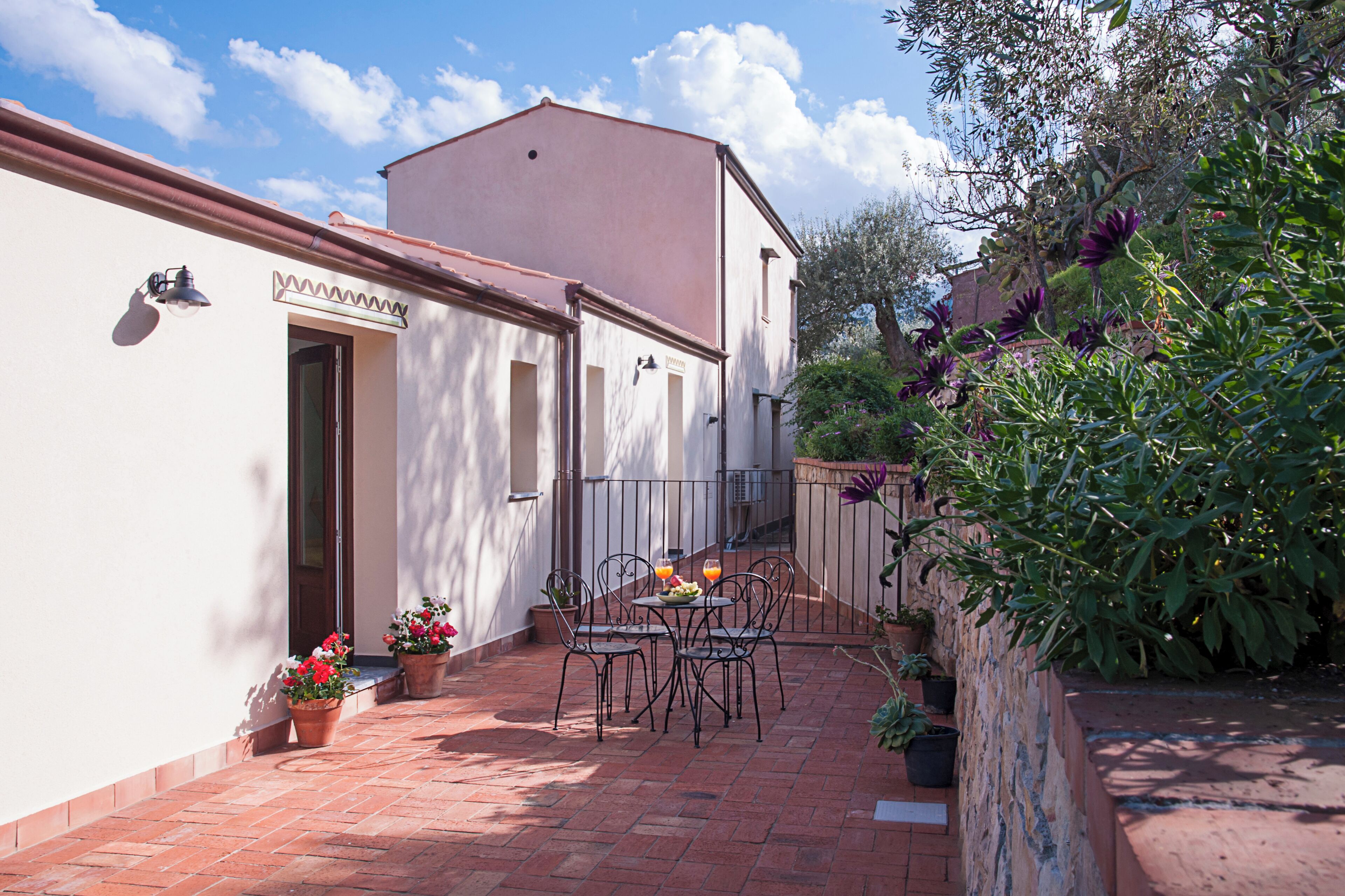Une terrasse avec une table et des chaises, des plantes en pot et un bâtiment sur lequel est apposée une enseigne.