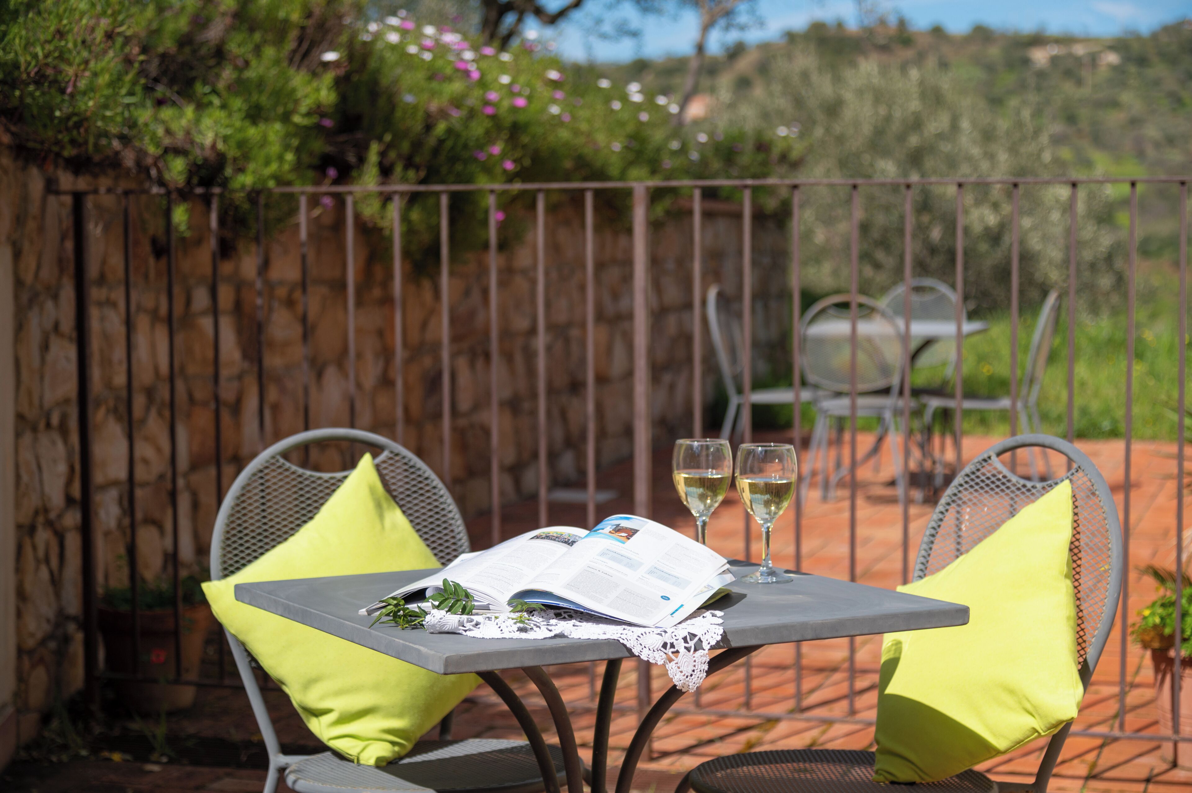 A patio with a table set for two, featuring a book and two glasses of wine.
