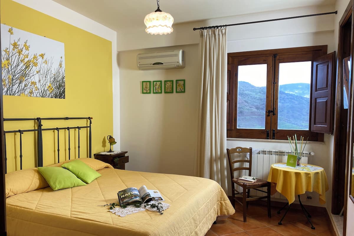 Quarto com cama, janela com cortinas, mesa e uma cadeira, e radiador.