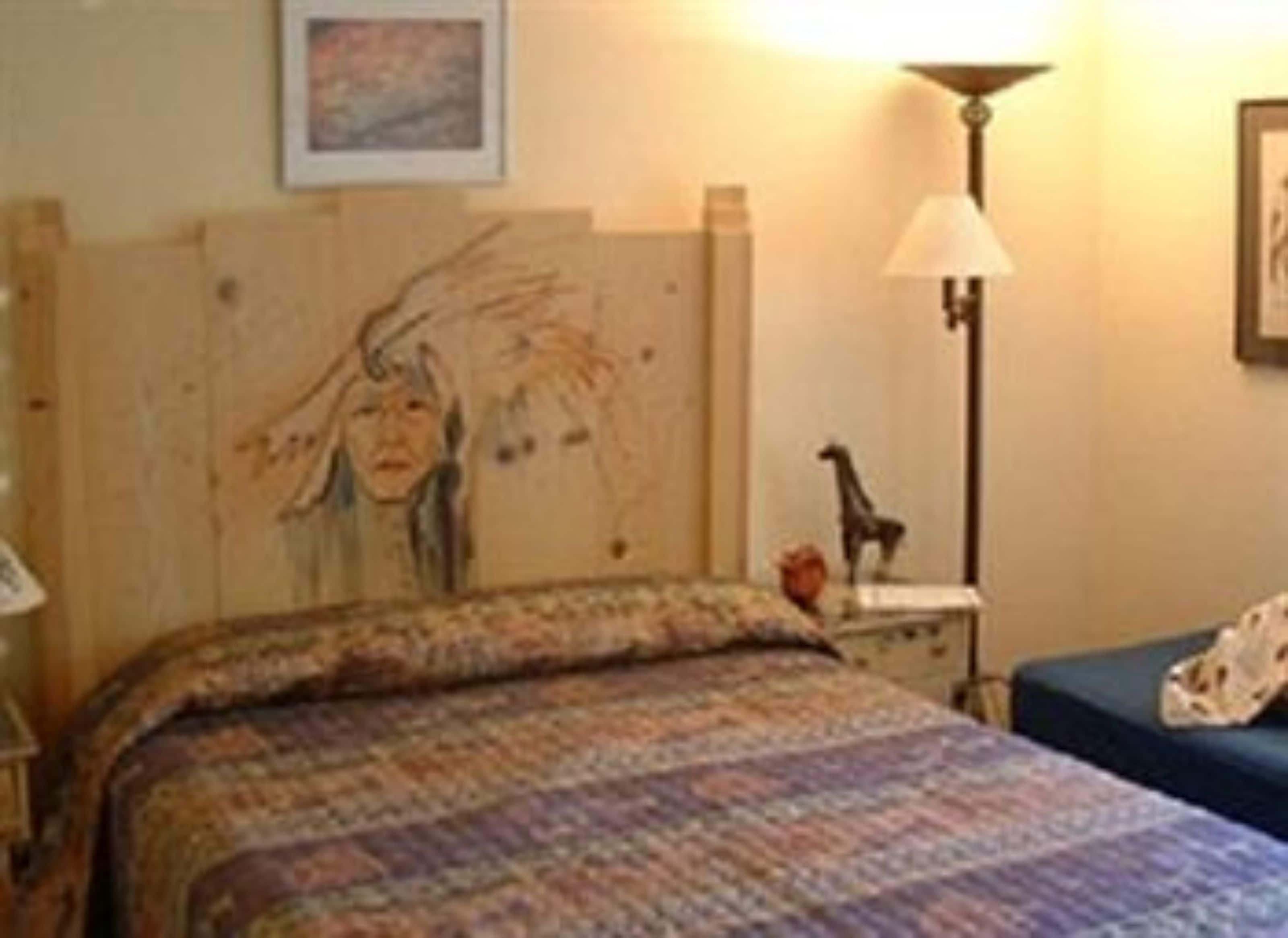A room with a bed, a lamp, a giraffe figurine, and a painting on the wall.