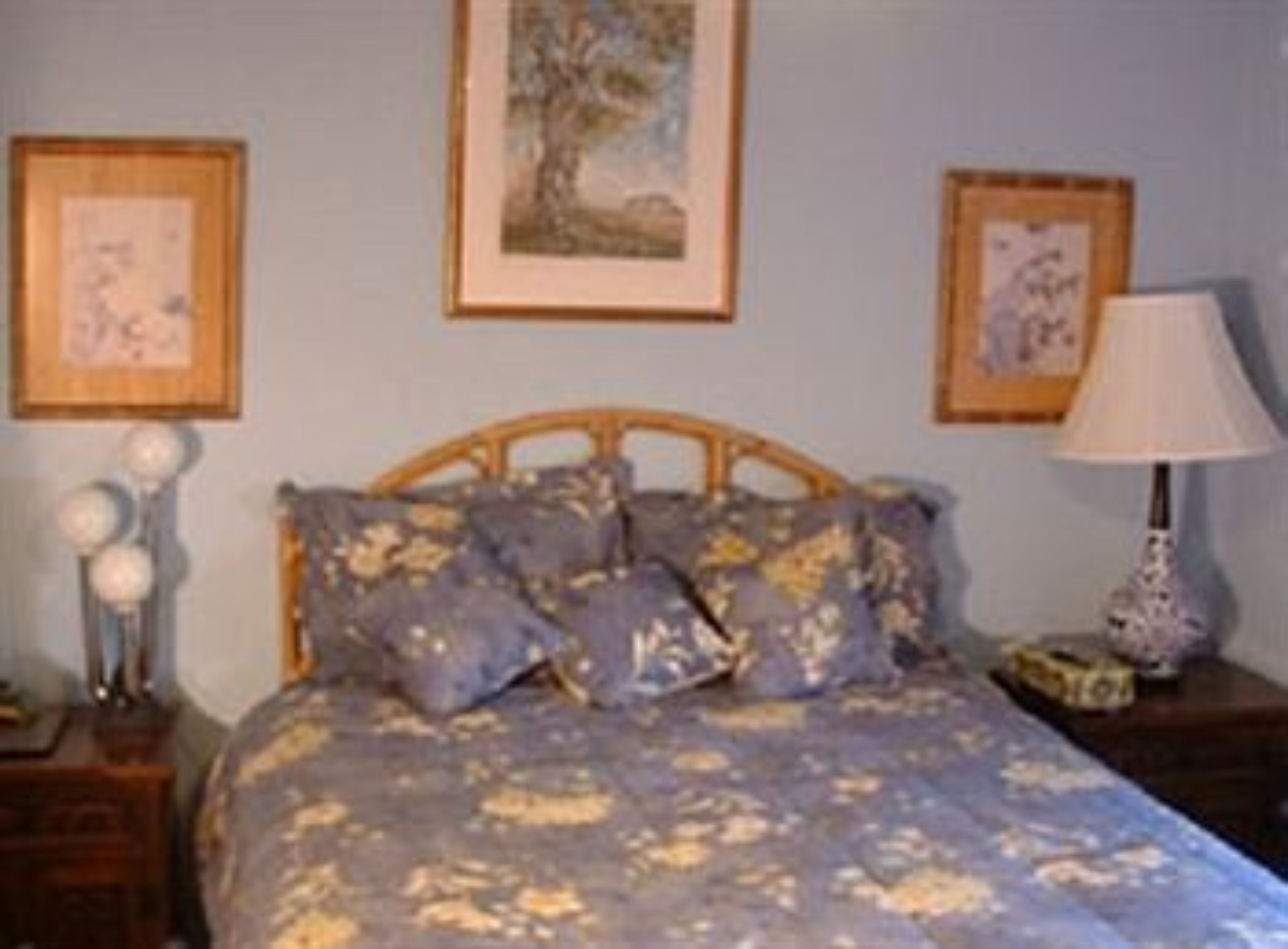 Un dormitorio con cama, cuadros en la pared, una mesita de noche y una lámpara.