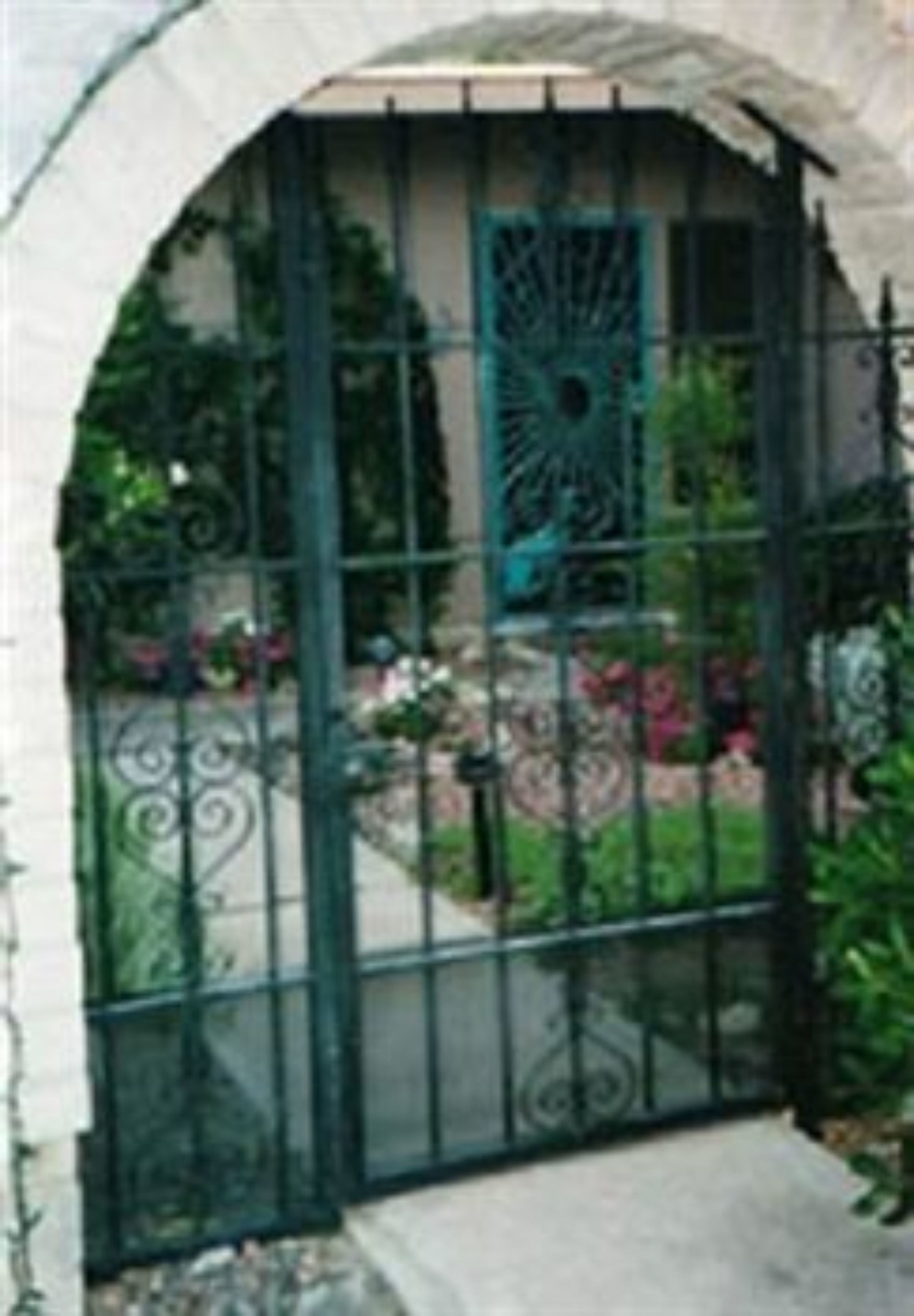 Una entrada cerrada con un portón metálico decorativo y una puerta verde, que da paso a un jardín ajardinado.